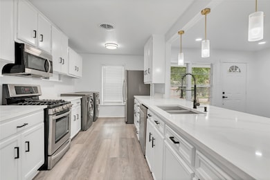 Kitchen featuring stainless steel appliances, white cabinetry, pendant lighting, light wood-style flooring, and light stone counters