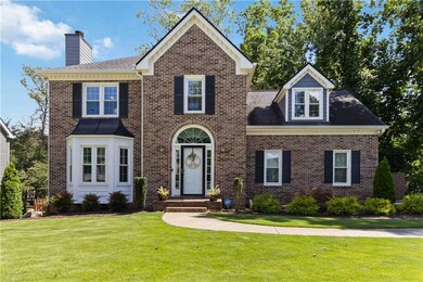 Colonial-style house featuring a chimney, brick siding, a front yard, and a shingled roof
