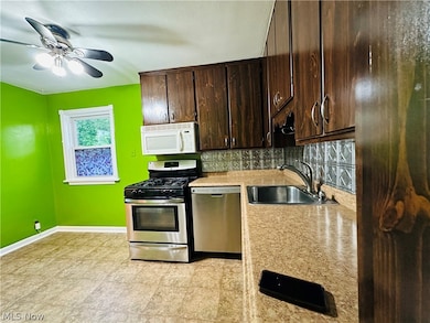 Kitchen featuring backsplash, dark brown cabinets, light countertops, light tile floors, and stainless steel appliances