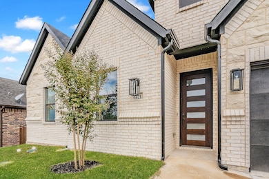 Doorway to property featuring brick siding, a lawn, and a shingled roof