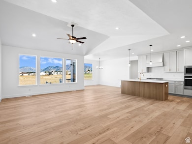Kitchen featuring open floor plan, white cabinets, a ceiling fan, a center island with sink, and a chandelier