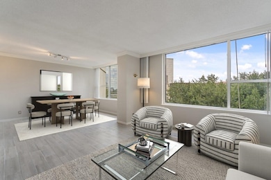 Living room opens to dining room with verdant views and large windows. Virtually staged.