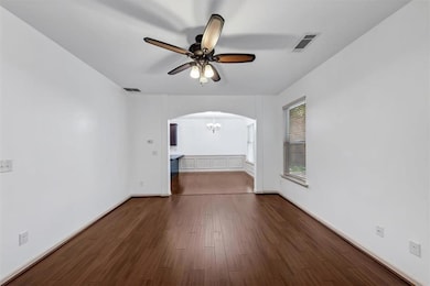 Empty room with arched walkways, ceiling fan, a chandelier, and dark wood-style flooring