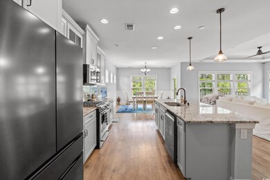 Kitchen with stainless steel appliances, recessed lighting, white cabinets, light wood-type flooring, and a kitchen island with sink