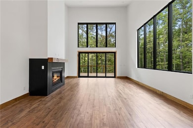 Unfurnished living room with healthy amount of natural light, wood-type flooring, a glass covered fireplace, and a high ceiling