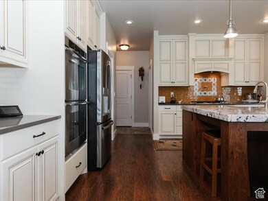 Kitchen with decorative backsplash, decorative light fixtures, appliances with stainless steel finishes, white cabinets, and dark wood-type flooring