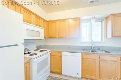 Kitchen with white appliances, light brown cabinetry, light tile patterned floors, and light stone countertops