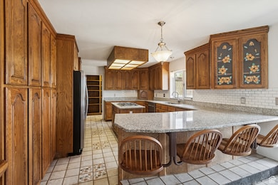 Kitchen with hanging light fixtures, a peninsula, light stone countertops, light tile patterned floors, and brown cabinets