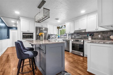 Kitchen featuring stainless steel appliances, under cabinet range hood, white cabinetry, a kitchen island, and a textured ceiling