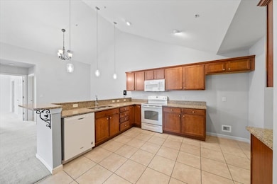 Kitchen featuring white appliances, brown cabinets, a peninsula, high vaulted ceiling, and light stone countertops