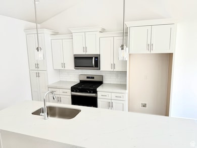 Kitchen with appliances with stainless steel finishes, light stone countertops, white cabinets, tasteful backsplash, and vaulted ceiling
