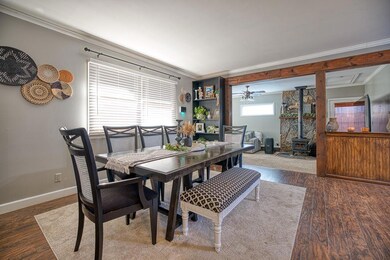 Dining area with ornamental molding, a wood stove, and wood finished floors