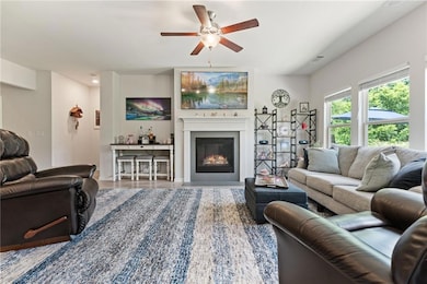 Living area with a ceiling fan, a glass covered fireplace, and wood finished floors