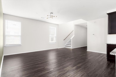 Unfurnished living room with dark wood finished floors, stairway, and a chandelier