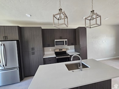 Kitchen with appliances with stainless steel finishes, a center island with sink, decorative light fixtures, and sink