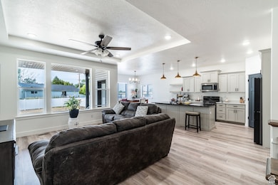 Living room with a textured ceiling, ceiling fan, a tray ceiling, light wood-style flooring, and a chandelier