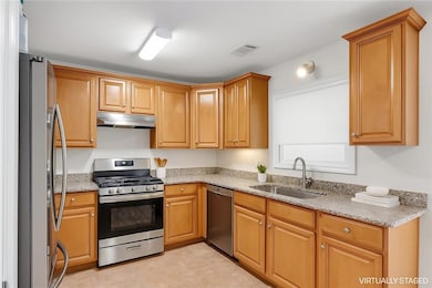 Kitchen featuring stainless steel appliances, under cabinet range hood, light stone counters, and light tile patterned floors