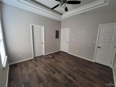 Empty room with a raised ceiling, a ceiling fan, dark wood finished floors, and electric panel