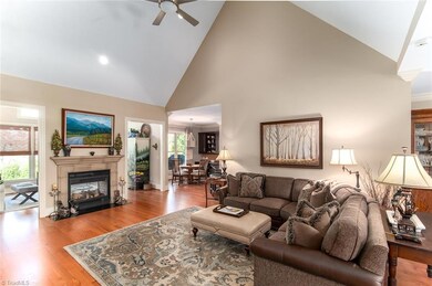 Living room with vaulted ceiling, hardwood flooring and a double sided fireplace with gas logs also open to the sunroom.