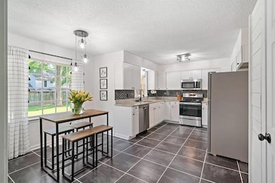 Kitchen with appliances with stainless steel finishes, decorative backsplash, white cabinetry, a textured ceiling, and dark tile patterned flooring