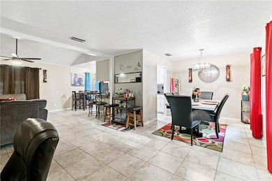 Dining space featuring a textured ceiling, light tile patterned floors, vaulted ceiling, and ceiling fan
