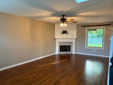 Unfurnished living room with a ceiling fan, wood finished floors, a stone fireplace, a textured ceiling, and a skylight