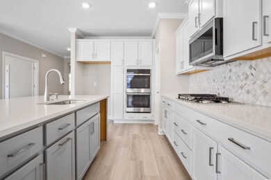 Kitchen featuring backsplash, ornamental molding, stainless steel appliances, light wood-style flooring, and white cabinets