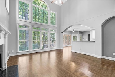 Unfurnished living room featuring ceiling fan, a fireplace, a high ceiling, arched walkways, and dark wood-type flooring