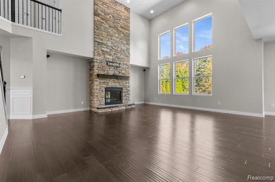 Unfurnished living room featuring a high ceiling, dark wood finished floors, and a stone fireplace