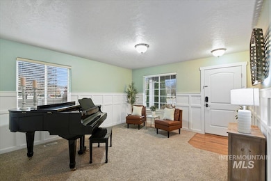Sitting room featuring a textured ceiling, light colored carpet, a decorative wall, and a wainscoted wall