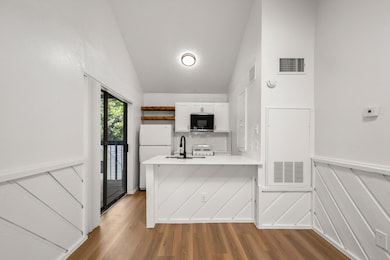 Kitchen featuring a wainscoted wall, a decorative wall, vaulted ceiling, light wood-style flooring, and white appliances