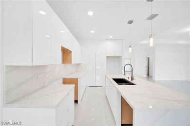 Kitchen with white cabinetry, decorative light fixtures, tasteful backsplash, sink, and light stone countertops