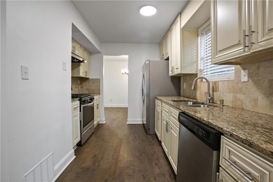 Kitchen featuring backsplash, dark stone counters, stainless steel appliances, dark wood finished floors, and cream cabinetry