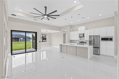 Kitchen with open floor plan, light marble finish flooring, appliances with stainless steel finishes, a raised ceiling, and white cabinets