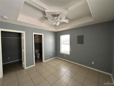 Unfurnished bedroom featuring a raised ceiling, electric panel, a spacious closet, and tile patterned flooring