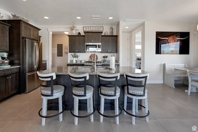 Kitchen featuring dark brown cabinets, stainless steel appliances, a kitchen island with sink, light tile patterned floors, and recessed lighting