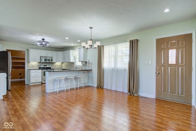 kitchen with light wood-type flooring, a notable chandelier, backsplash, stainless steel appliances, and a peninsula