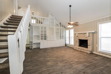 Unfurnished living room with stairs, dark wood-type flooring, ceiling fan, a stone fireplace, and a towering ceiling