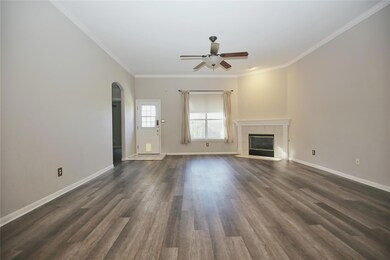 Unfurnished living room featuring ornamental molding, a tiled fireplace, dark wood-style floors, arched walkways, and ceiling fan