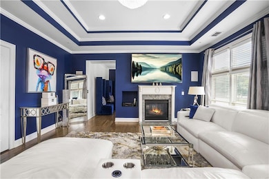Living room with wood finished floors, a raised ceiling, a fireplace, and ornamental molding