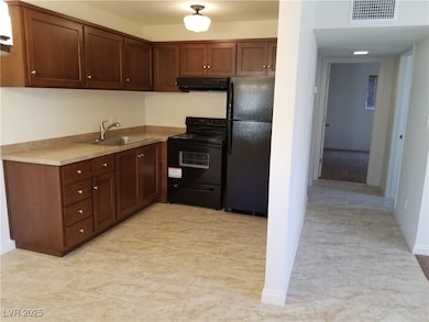 Kitchen with light countertops, exhaust hood, black appliances, visible vents, and a sink