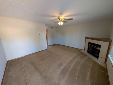 Unfurnished living room with a fireplace, carpet, a ceiling fan, and a textured ceiling