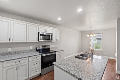 Kitchen with stainless steel appliances, dark wood-style floors, light stone countertops, a center island with sink, and pendant lighting