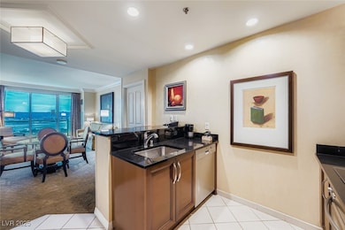 Kitchen featuring a peninsula, light tile patterned flooring, dark stone countertops, dishwasher, and brown cabinetry