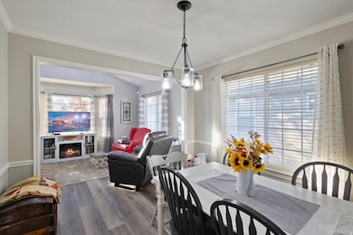 Dining space featuring wood finished floors, a warm lit fireplace, ornamental molding, and a chandelier