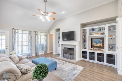 Living room featuring light wood-type flooring, a premium fireplace, vaulted ceiling, built in shelves, and ornamental molding
