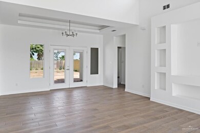 Empty room featuring french doors, light hardwood / wood-style flooring, a high ceiling, a notable chandelier, and a raised ceiling