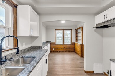 Kitchen featuring white cabinetry, light wood-type flooring, under cabinet range hood, and dark stone countertops