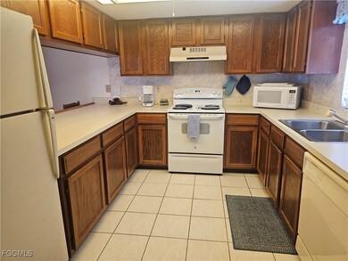 Kitchen with white appliances, light countertops, under cabinet range hood, light tile patterned flooring, and brown cabinetry