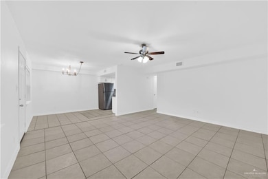 Empty room with baseboards, visible vents, light tile patterned floors, and ceiling fan with notable chandelier